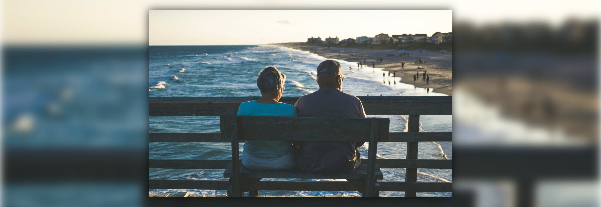 Couple de personnes âgées assis sur un banc en bois face à l'océan, le dos tourné, contemplant la Côte de Jade au coucher de soleil.
